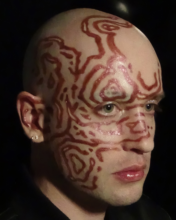 Close up portrait of Jesse with swirling maroon pattern makeup against a black background